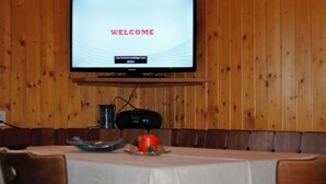 Ein Konferenzraum mit Tisch, Stühlen, einem Fernseher, der 'WELCOME' anzeigt, und einer Holzwand.