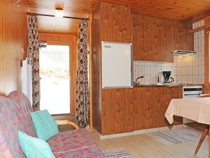 A compact living space with a sofa, a dining table, a kitchenette, and a door leading to an outdoor area.