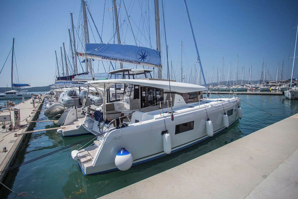 A marina with multiple yachts docked, a clear sky, and a calm water surface.