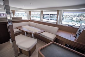 A compact boat interior with a dining area, seating, and a view of a marina. - Sun-Kissed Sailing Adventure in Islas Baleares, Mallorca (Palma)