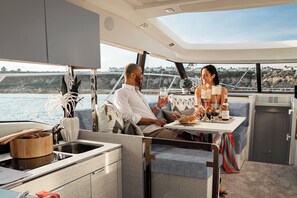 Interior de un yate con comedor, cocina y vistas al mar.