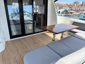 Un balcón con zona de estar acolchada, una mesita y vistas a un puerto deportivo con barcos.