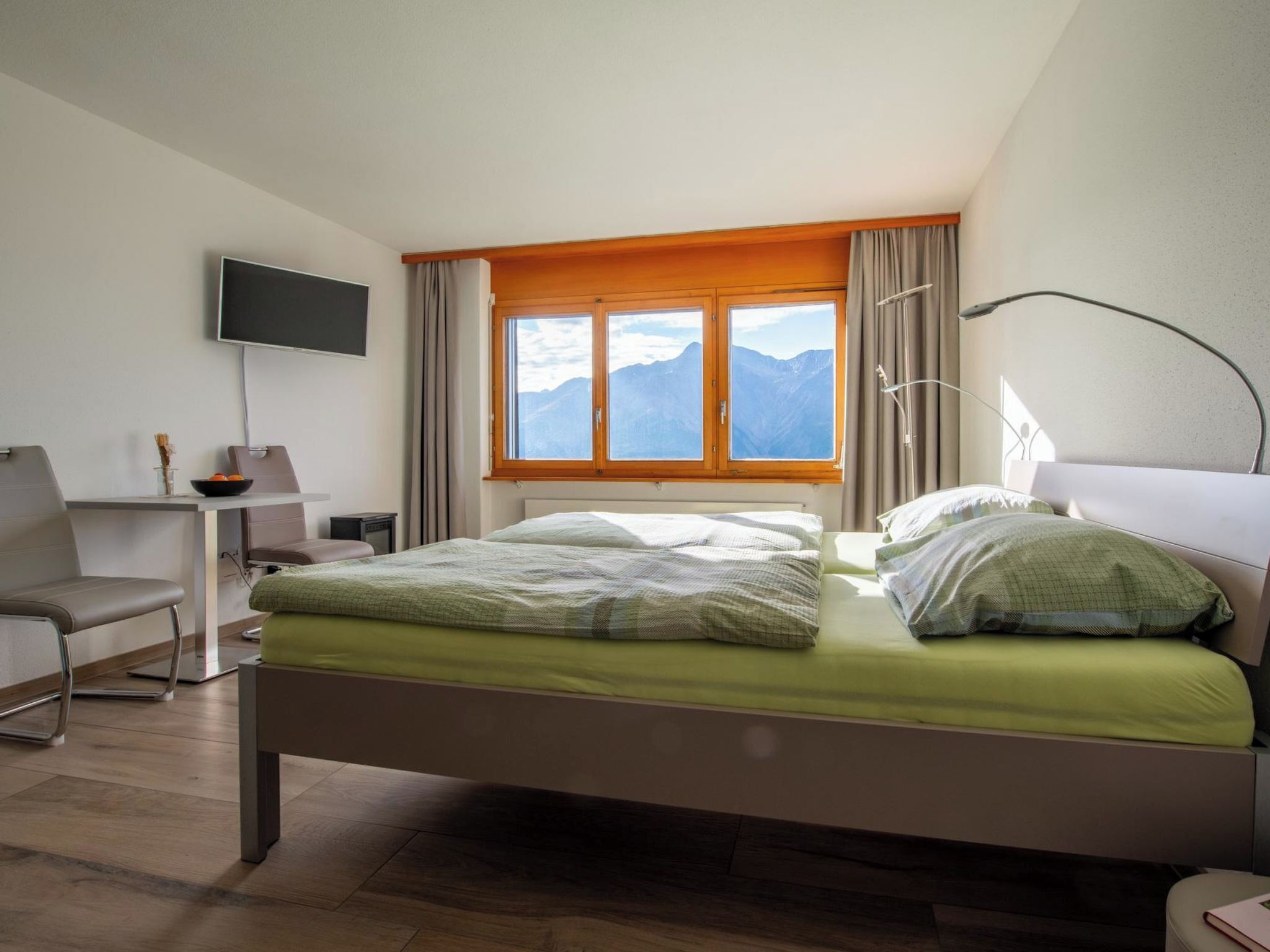 A hotel room with a bed, a desk, a chair, a TV, and a window with a mountain view.