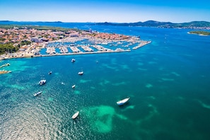 Luftaufnahme einer Küstenstadt mit einer Marina, Booten und tiefblauem Meer.