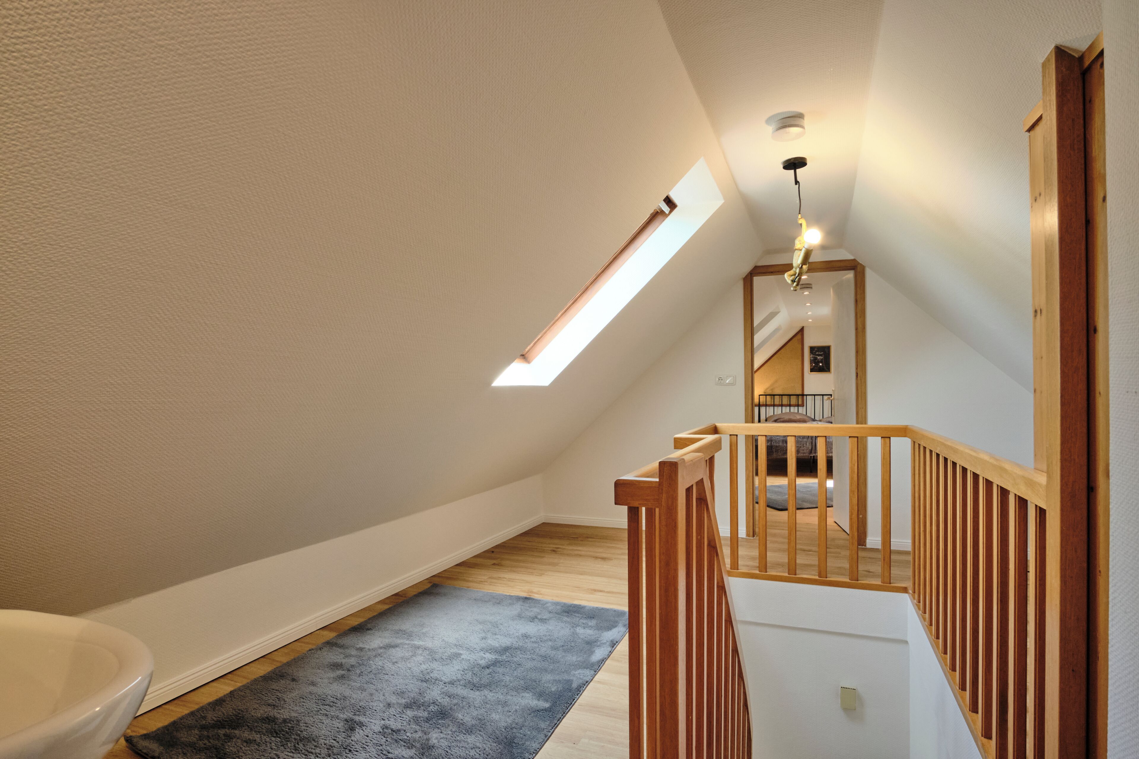 Un dormitorio estilo loft moderno con tragaluces, escalera de madera y vista de la habitación contigua.