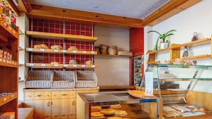 A bakery interior with wooden shelves displaying bread, a display case with pastries, and wicker baskets.