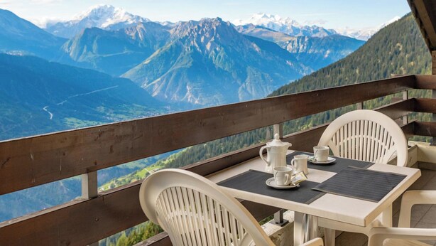 A table with chairs on a balcony overlooking a mountainous landscape.