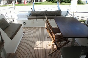 A boat deck with a wooden table, cushioned seating, and a small white table.