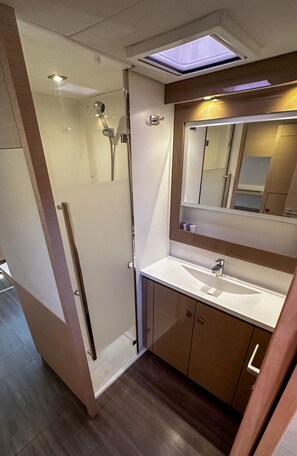 A modern bathroom with a glass shower enclosure, a vanity with a mirror, and a skylight above the sink. - Sun-Kissed Sailing Adventure in Sibenik, Croatia (Primošten)