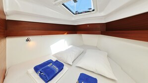Una cabina compatta con un lucernario, biancheria bianca e un asciugamano blu con la scritta 'ANGEL YACHT'.