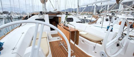 A boat deck with a steering wheel, a wooden floor, and a small table with a cushion.