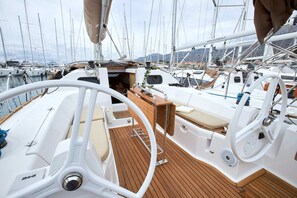 A boat deck with a steering wheel, a wooden floor, and a small table with a cushion. - Sun-Kissed Sailing Adventure in Split, Croatia (Kaštel Gomilica)