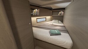 Ein gemütlicher, gut beleuchteter Raum mit einem Bett, einer kleinen Ablage mit Büchern und einem Fenster mit Ausblick.