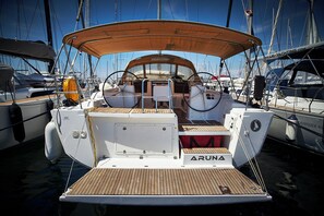 Eine Yacht namens 'ARUNA' liegt in einer Marina zusammen mit anderen Booten vor Anker und verfügt über ein Holzdeck sowie einen überdachten Sitzbereich.