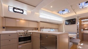 A compact kitchen with a built-in oven, a refrigerator, and a flat-screen TV mounted on the wall. - Sun-Kissed Sailing Adventure in Split, Croatia (Kaštel Gomilica)