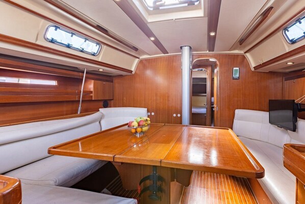 A boat interior with a wooden table, white cushioned seating, and a skylight.