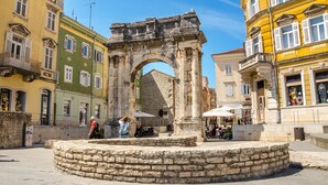 An ancient stone archway in a public square with surrounding buildings and outdoor seating. - Sun-Kissed Sailing Adventure in Istria, Croatia (Pula)