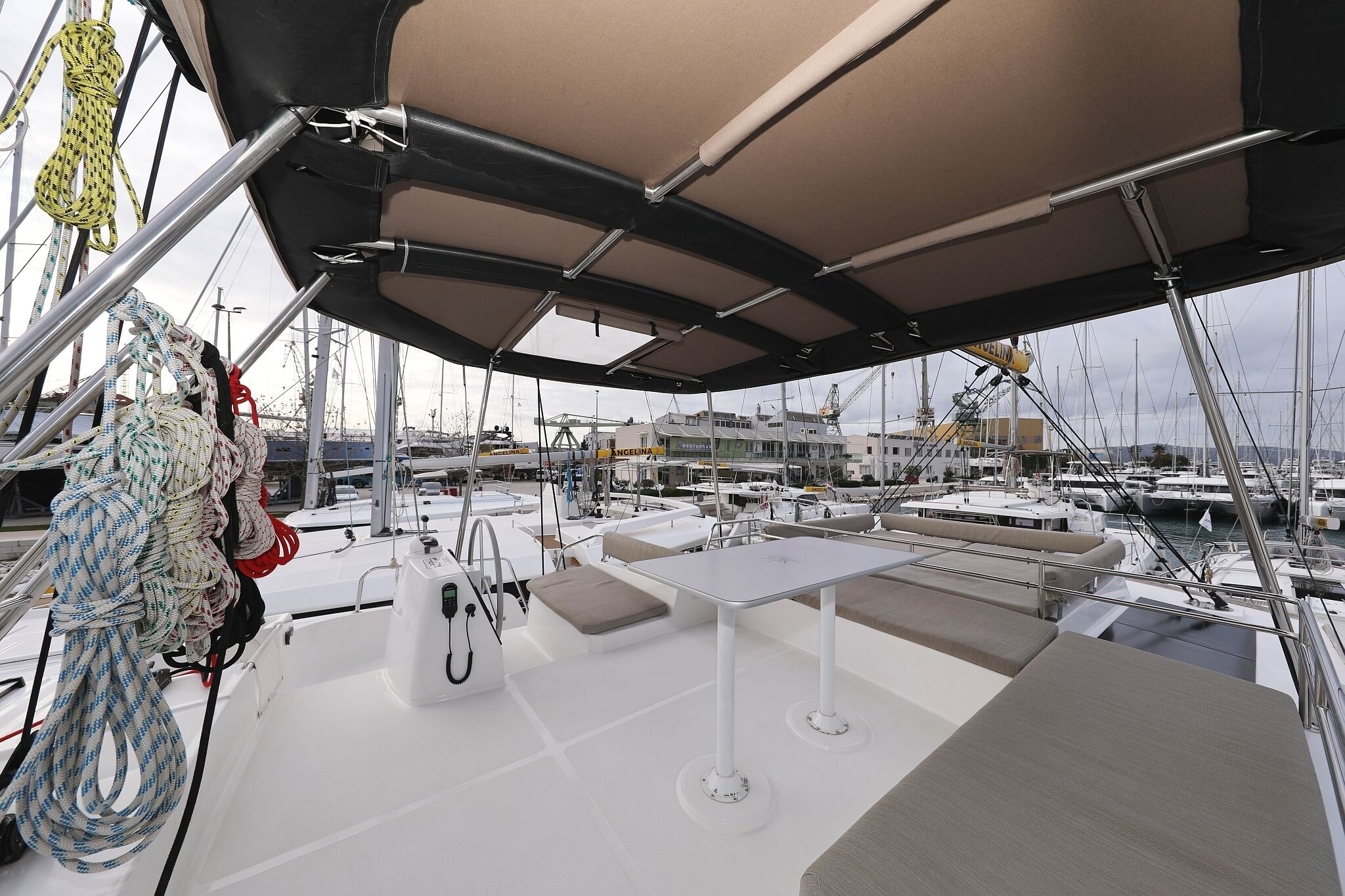 A covered deck area with seating and a table, ropes and rigging, and a marina with boats in the background.