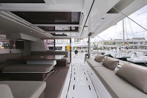 Interieur van een jacht met een eethoek, zitplaatsen en uitzicht op de jachthaven.