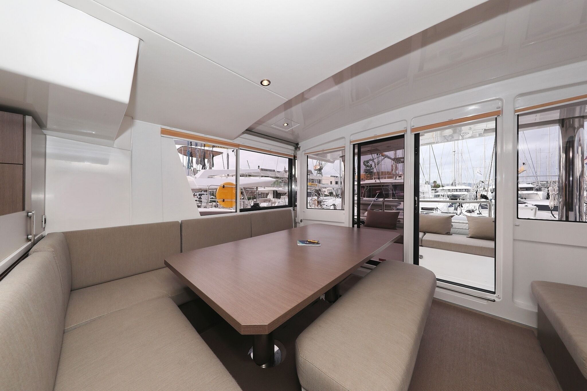 A modern interior with a central table, seating, and large windows offering views of boats.
