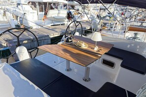 Cubierta de barco con timón, una mesa con un sombrero y una lámpara.