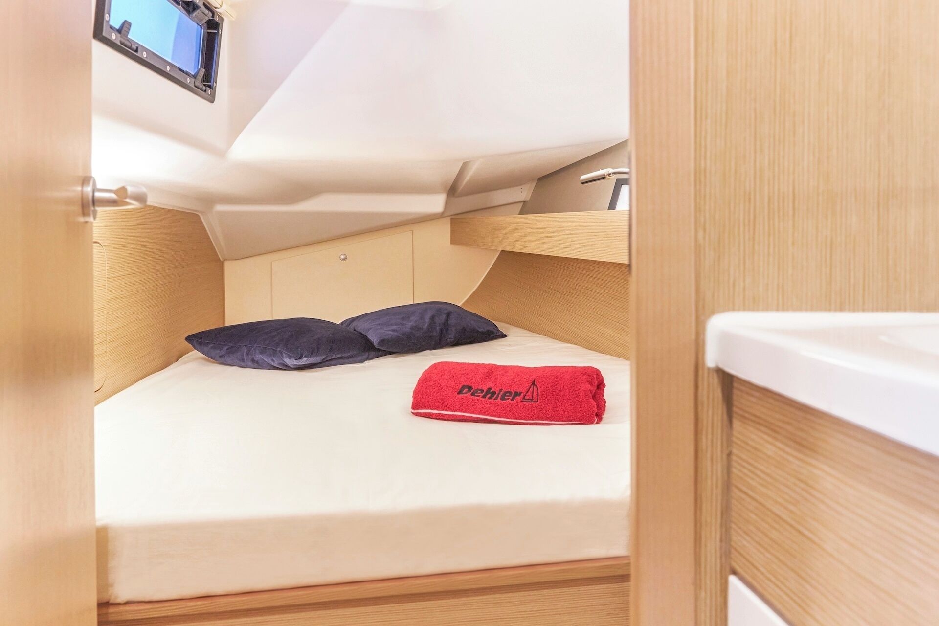 A compact boat cabin with a bed, a red towel, and a mounted television.