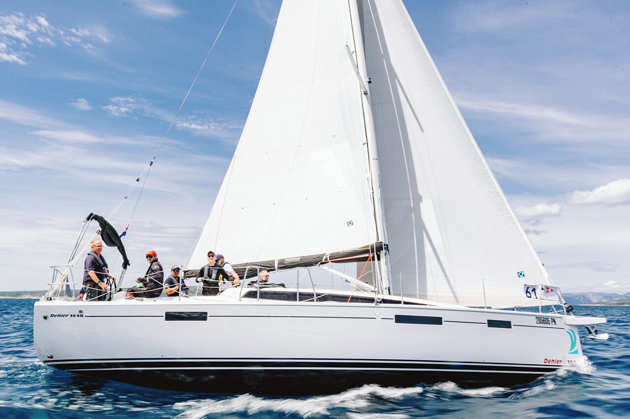 Un velero con casco blanco y una vela grande, que incluye una cabina con asientos y una bandera.