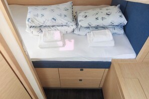 A bed with a white sheet and pillows, a blue headboard, and wooden storage drawers. - Sun-kissed Sailing Adventure in Split-Dalmatia, Croatia (Seget Donji)