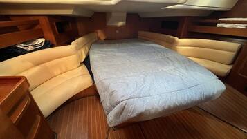 A compact boat interior with a foldable bed, wooden cabinetry, and a small seating area.
