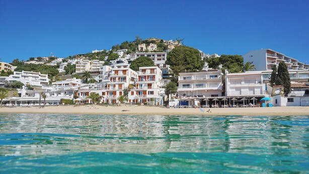 Un hôtel en bord de mer, avec plusieurs étages, situé directement sur la plage et offrant une vue sur des eaux d’un bleu limpide.