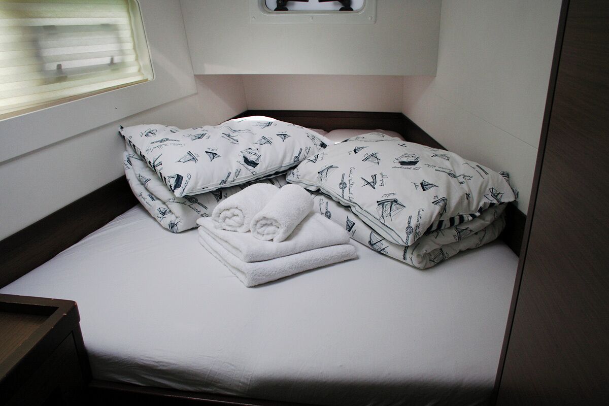 A small bed with white bedding and patterned pillows, a window with blinds, and a wooden headboard.