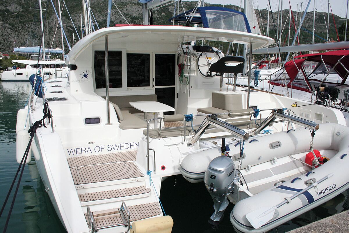 A white yacht named 'WERA OF SWEDEN' docked at a marina with a covered seating area, a small table, and a motor outboard.