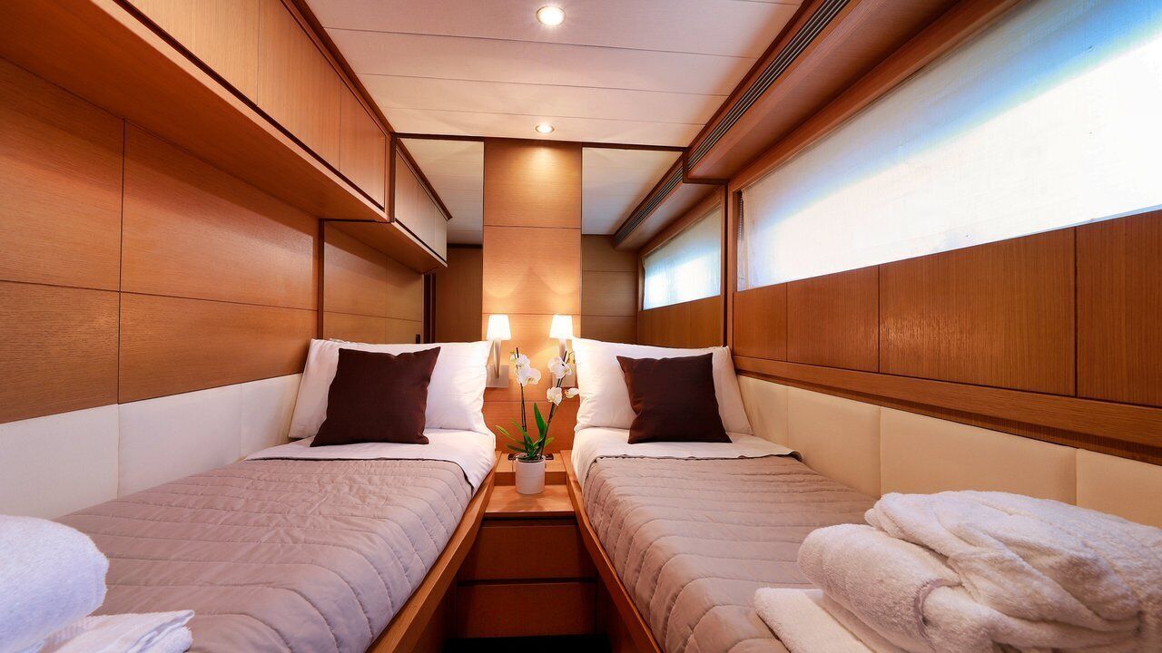 A hotel room with two beds, wooden headboards, a nightstand with a lamp, and a potted plant.