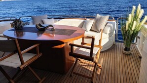 Ein Bootsdeck mit einem runden Holztisch, gepolsterten Sitzgelegenheiten und einem Blumentopf.