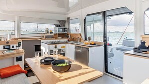 Uma cozinha compacta moderna com fogão, pia e área de estar, janelas amplas e vista para a água.