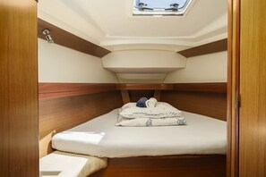 Ein gemütliches, helles Blockhaus mit Dachfenster, einem Bett mit ordentlich zusammengelegtem Handtuch und einer kleinen Sitzecke.