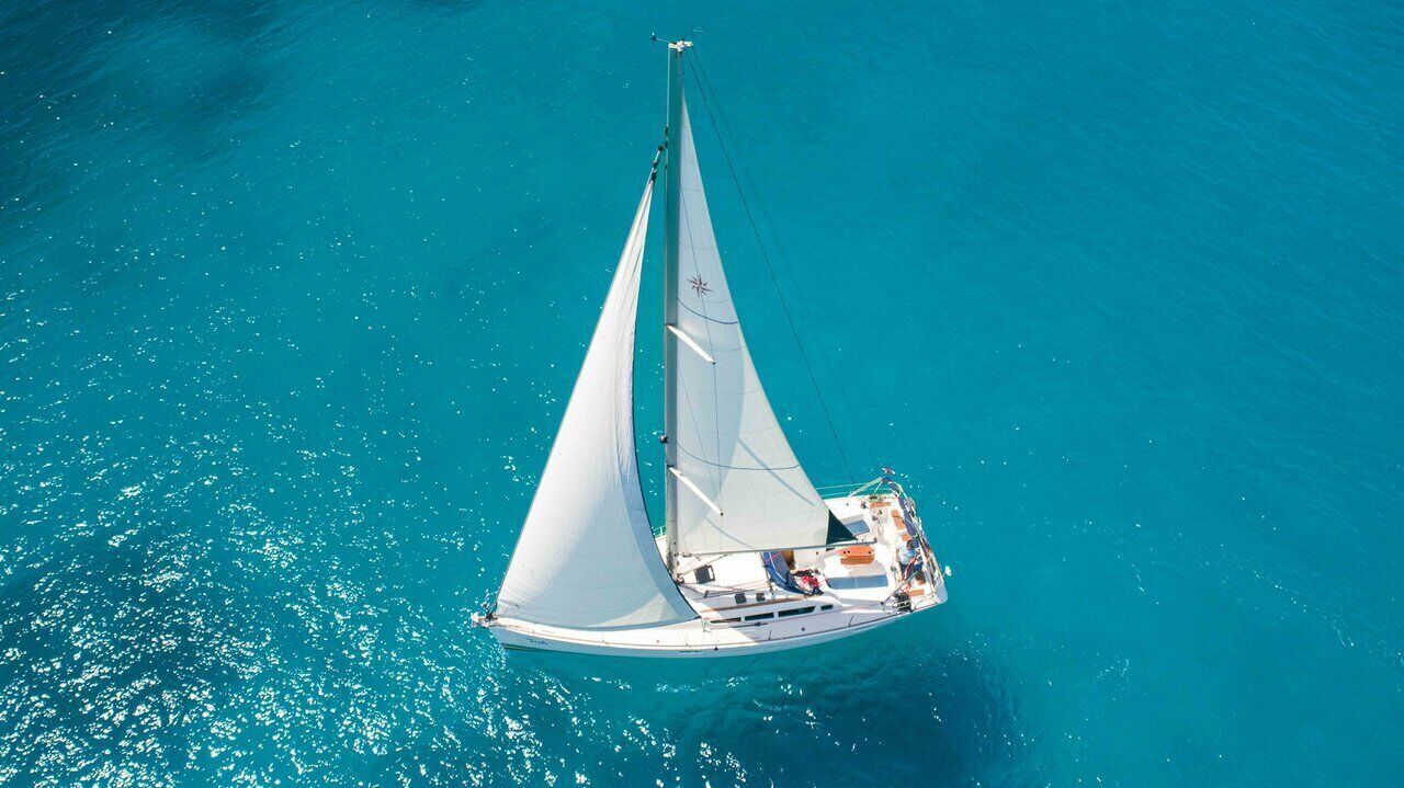 Un voilier à la coque et aux voiles blanches, flottant sur une eau turquoise.