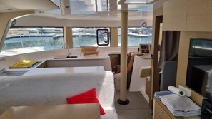 Bådens indre viser en seng, et lille bord, en stol, et kontrolpanel og udsigt til lysthavnen.