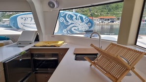 A compact kitchen with a stove, sink, and drying rack, overlooking a marina with boats. - Sun-Kissed Sailing Adventure in Northern Croatia (Punat)