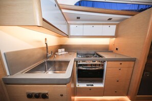 Een kleine keuken met een spoelbak, fornuis, oven en houten kastjes.