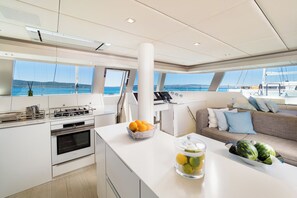 A modern kitchen with a view of the sea, a dining area with a sofa, and a large window. - Sun-Kissed Sailing Adventure in Split, Croatia (Kaštel Gomilica)
