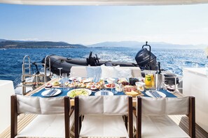 Une table à manger dressée avec différents plats, un moteur hors-bord Yamaha, et une vue sur la mer et les montagnes.