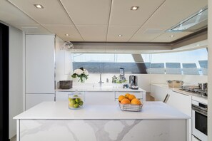 Une cuisine moderne dotée d’un plan de travail en marbre, d’un évier et offrant une vue sur la mer.
