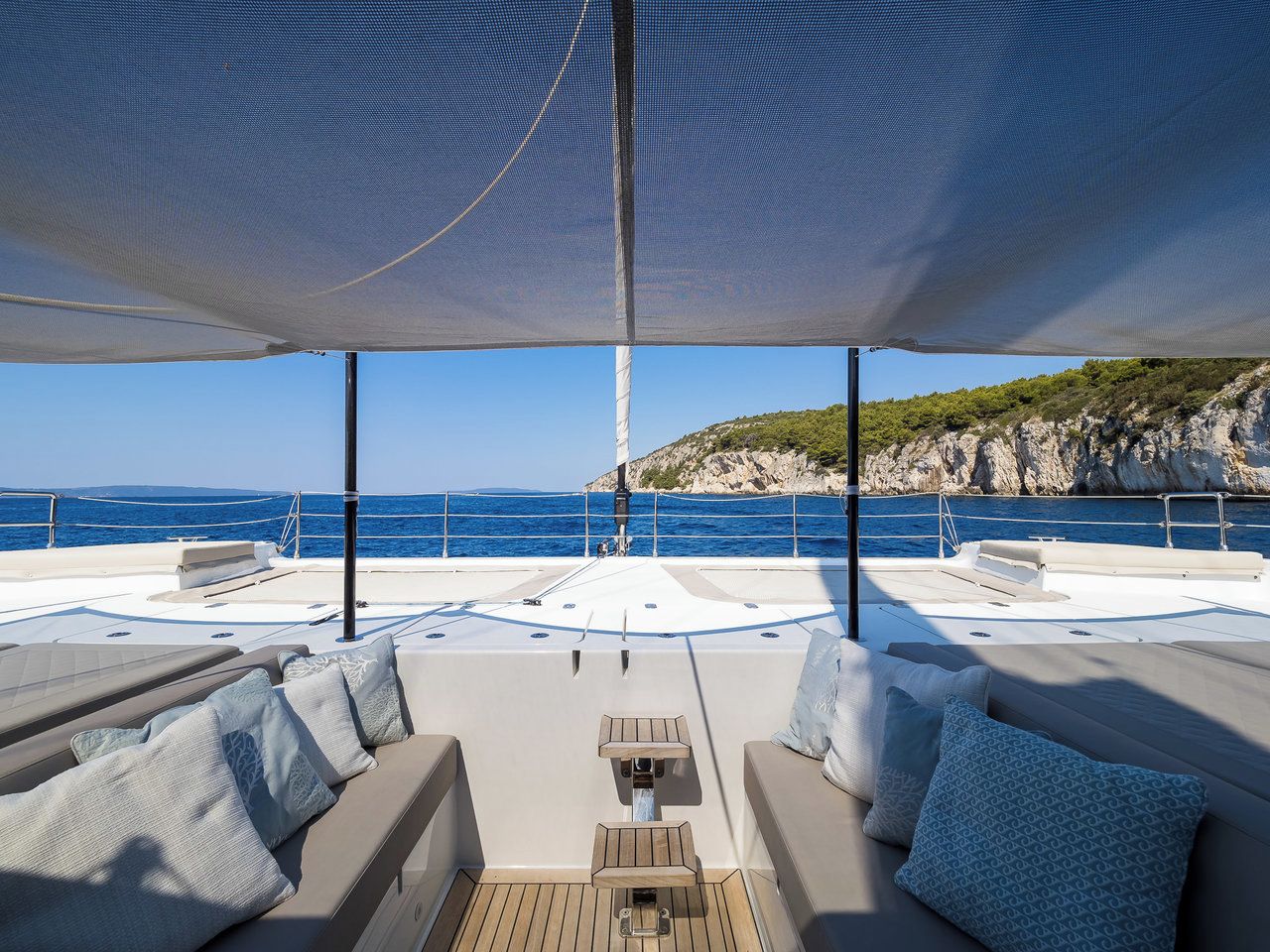A yacht deck with seating, a table, and a view of the sea and rocky coastline.