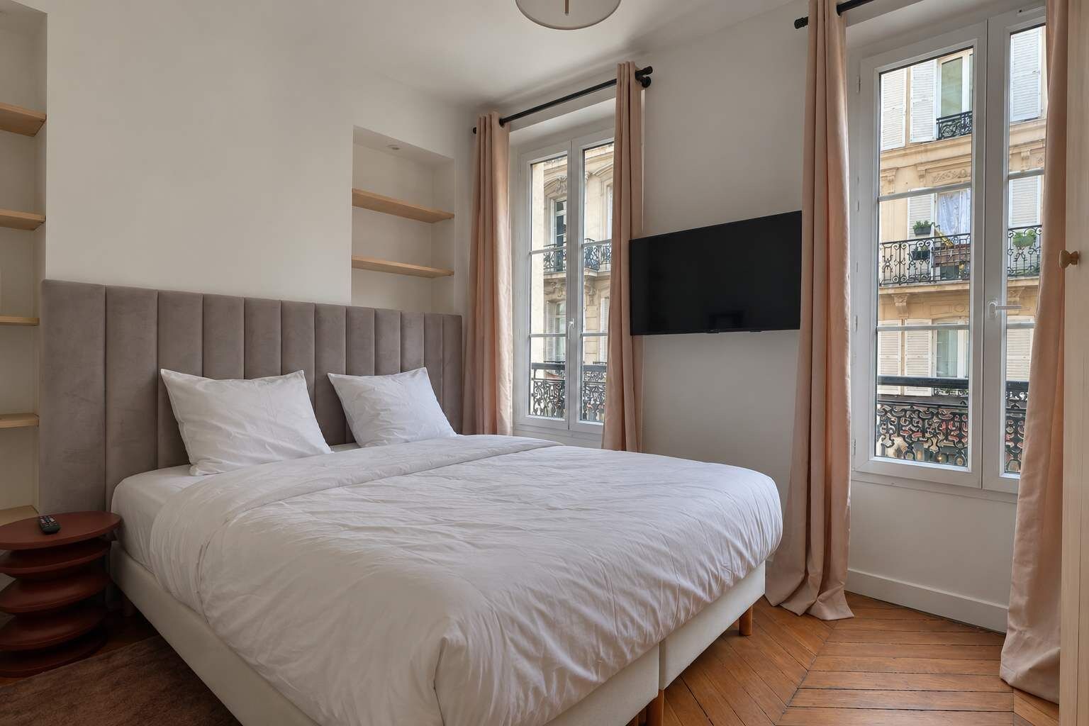 A bedroom with a bed, a TV mounted on the wall, and a window with curtains.