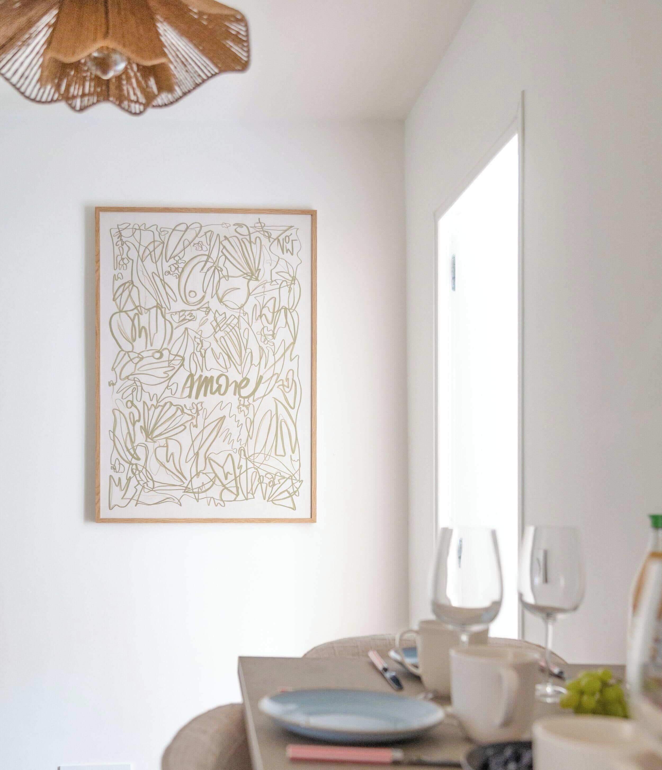 A dining area with a table, chairs, a framed artwork, and a hanging light fixture.