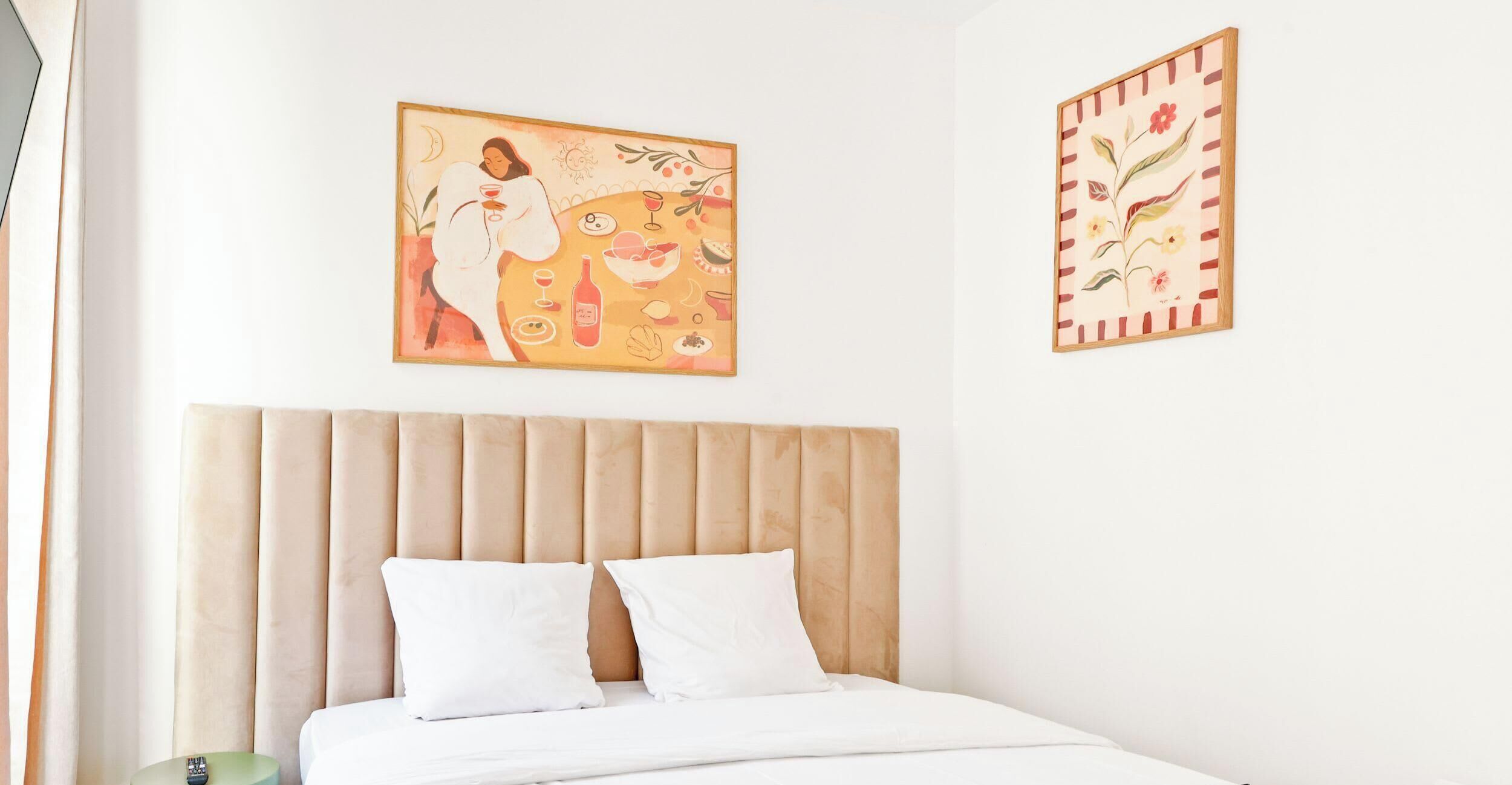 Un dormitorio con cama, dos almohadas, cabecera y dos obras de arte colgadas en la pared.