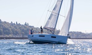 Un voilier sur des eaux calmes, avec un paysage vallonné en arrière-plan.
