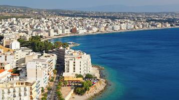 A coastal cityscape with a prominent beachfront hotel, a clear blue sea, and dense urban buildings.
