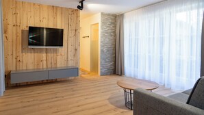 A modern living room with a flat-screen TV mounted on a wooden wall, a grey sofa, a round wooden coffee table, and a stone accent wall. - A beautiful apartment with its own terrace at Oberwinklgut. (Bischofshofen)